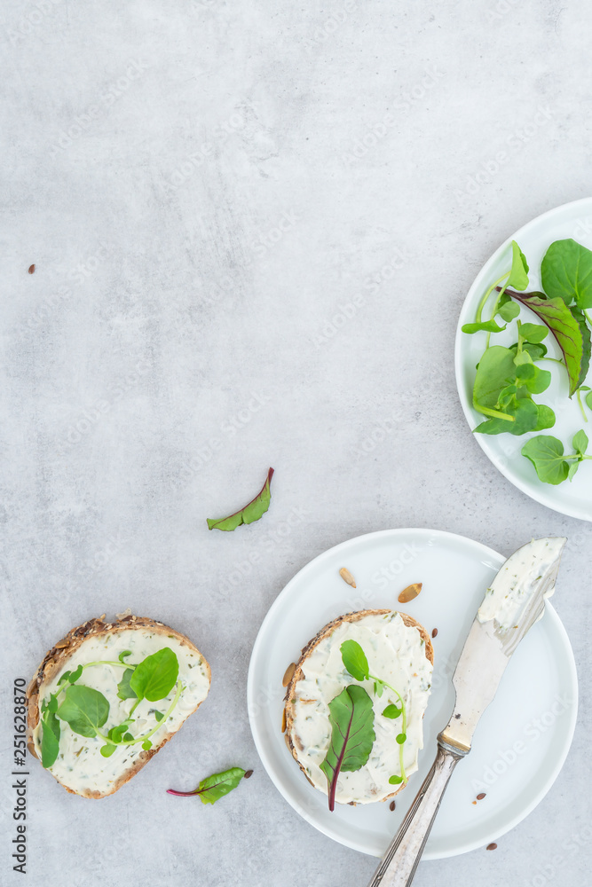Frisches Brot, mit veganem Frischkäse und Salat auf einem hellen Betonhintergrund