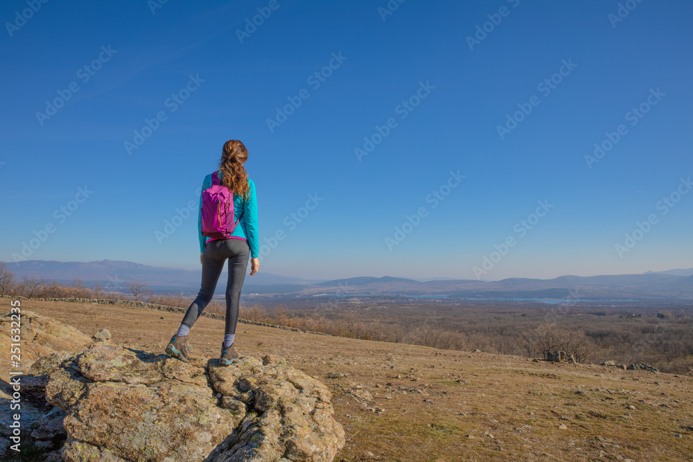 back of sport hiking or trekking woman standing on rock, looking at the valley, with text or copy space, in Guadarrama Natural Park (Madrid, Spain)