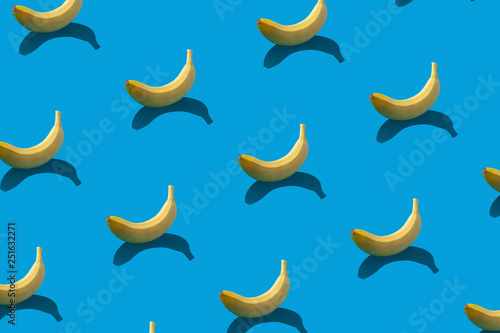 Pattern of yellow bananas with shadows on blue background.