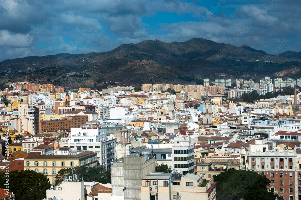 View of the Spanish city of Malaga from a height. Residential buildings, mountains, sights on the background of a cloudy sky.