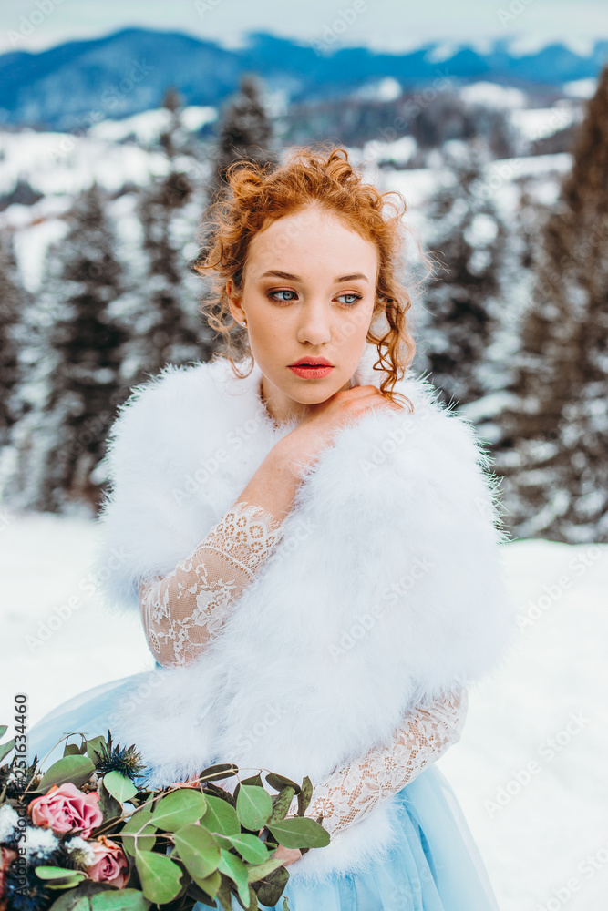 Attractive red-haired girl with a bouquet in her hands sitting on a chair against the backdrop of winter mountains Attractive red-haired girl with a bouquet in her hands sitting on a chair against the backdrop of winter mountains
