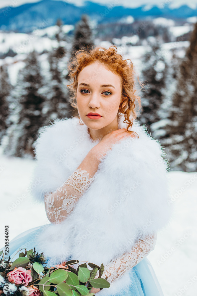 Cute red-haired girl with a bouquet in her hands sitting on a chair against the backdrop of winter mountains Cute red-haired girl with a bouquet in her hands sitting on a chair against the backdrop of winter mountains