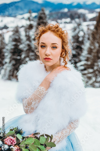 Cute red-haired girl with a bouquet in her hands sitting on a chair against the backdrop of winter mountains