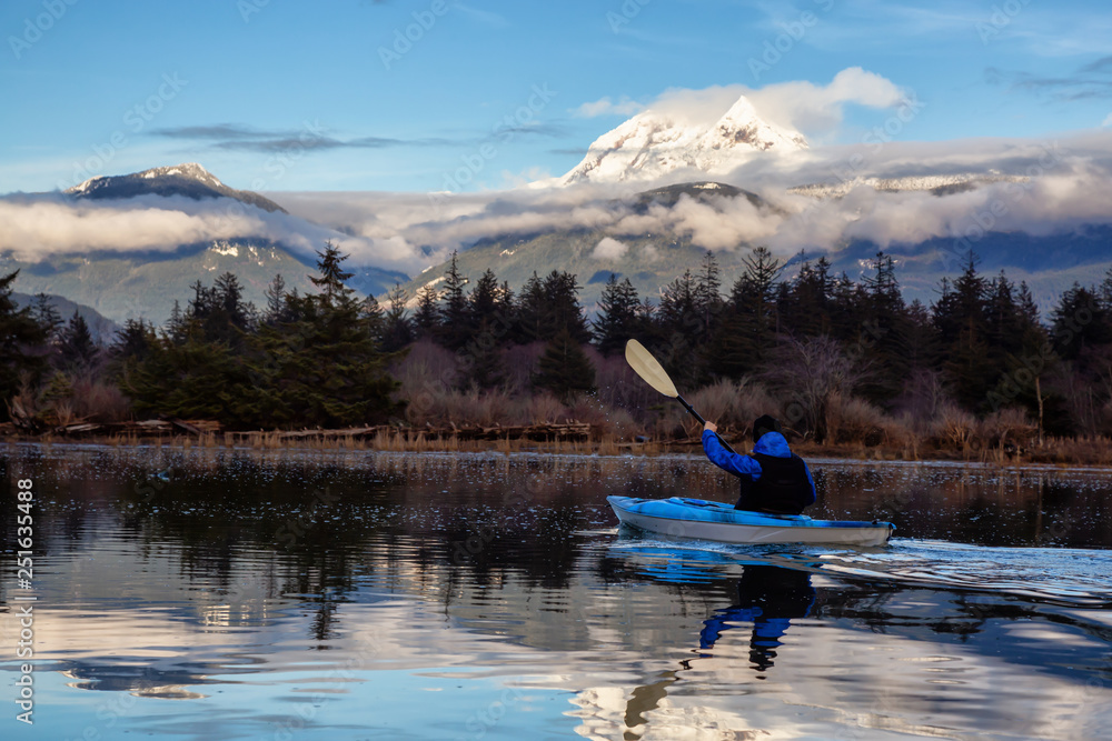 Adventurous man kayaking in peaceful water during a cloudy winter day. Taken in Squamish, North of Vancouver, BC, Canada.