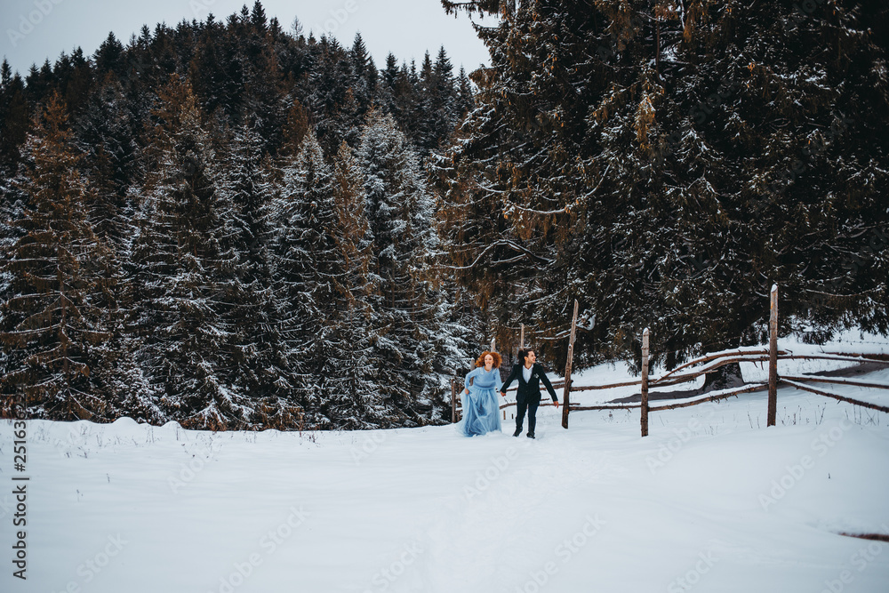 Bright couple walking in the snowy forest in the mountains