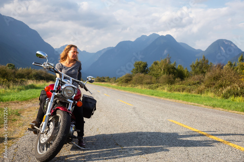 Woman riding a motorcycle on a scenic road surrounded by Canadian Mountains. Taken in Pitt Meadows  Greater Vancouver  BC  Canada.