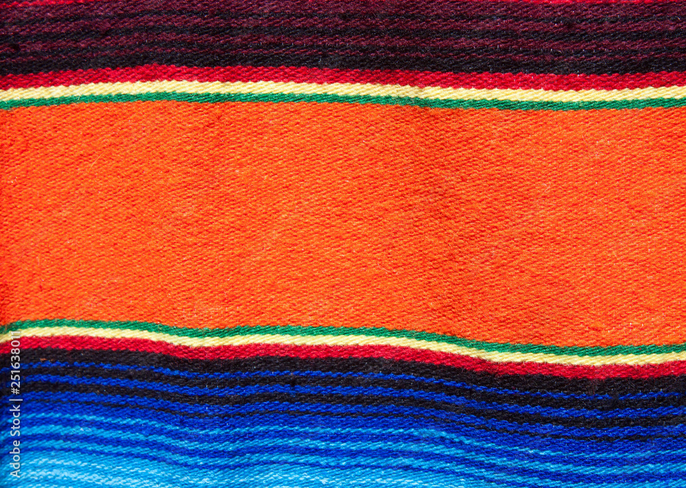 Obraz premium Multicolored cotton blanket with southwestern patterns from a market in Santa Fe, New Mexico, USA. One primary orange band in middle, other smaller bands are yellow and green and blue.