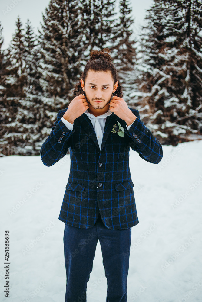 A handsome man with wavy hair in a suit stands in a winter forest A handsome man with wavy hair in a suit stands in a winter forest