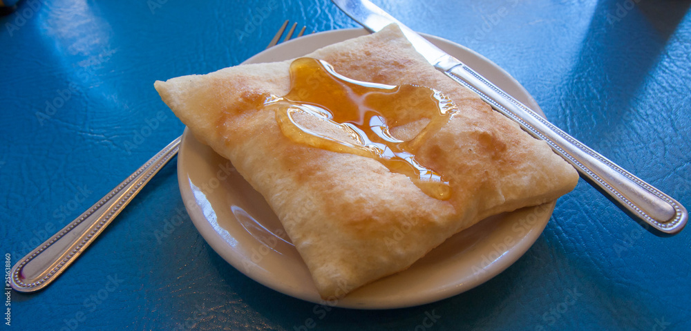 Naklejka premium Sopapilla. Zbliżenie, kolorowe zdjęcie sopapilla z restauracji w Santa Fe, Nowy Meksyk, USA. Jest to południowo-zachodni deser, który jest pustym kwadratowym kawałkiem smażonego ciasta z miodem na wierzchu