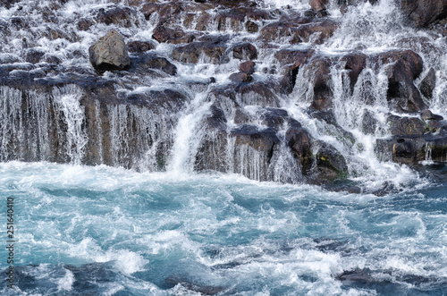 Wild waters (blue) and waterfall cascading over brown rocks, Hraunfossar, Iceland