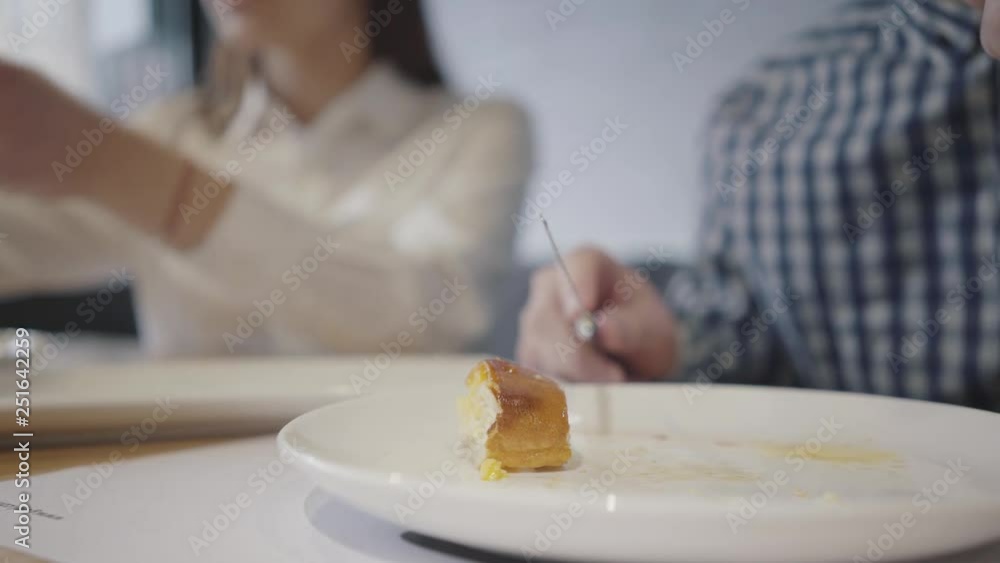 Unrecognizable couple having food in modern cafe close up. Man in the foreground eats pie with fork and knife, blurred woman figure is on the background. Man and woman spend time in restaurant Unrecognizable couple having food in modern cafe close up. Man in the foreground eats pie with fork and knife, blurred woman figure is on the background. Man and woman spend time in restaurant
