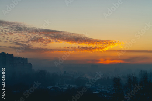 Cityscape with wonderful varicolored vivid dawn. Amazing peaceful cloudy sky above silhouettes of city buildings. Atmospheric background of orange sunrise. Sunset landscape. Copy space.