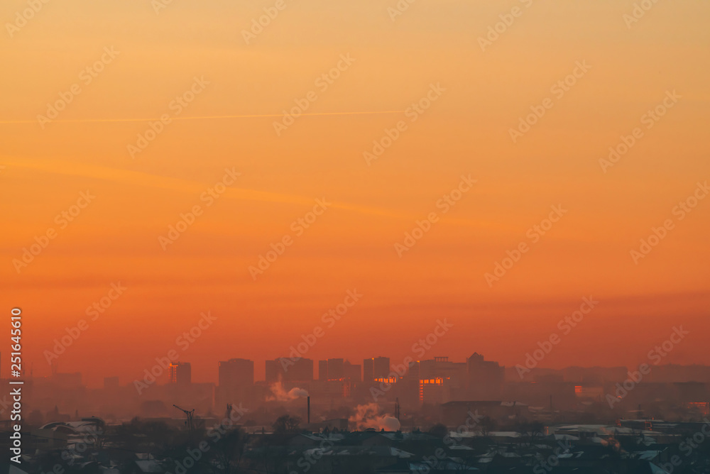 Urban high-rise buildings behind private houses on sunset. Silhouettes of big city buildings. Warm backlight of dawn. Private sector near apartment houses in sunlight. Minimalist cityscape at sunrise.