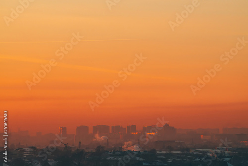 Urban high-rise buildings behind private houses on sunset. Silhouettes of big city buildings. Warm backlight of dawn. Private sector near apartment houses in sunlight. Minimalist cityscape at sunrise.