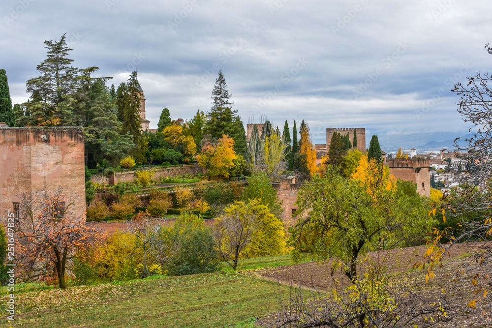 The high protective walls of a castle in southern Spain during the Fall or Autumn, with red and yellow leaves poking at it from all sides.