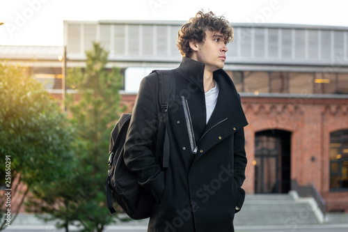 Close up of man in black coat passing through red bricked modern buildings.