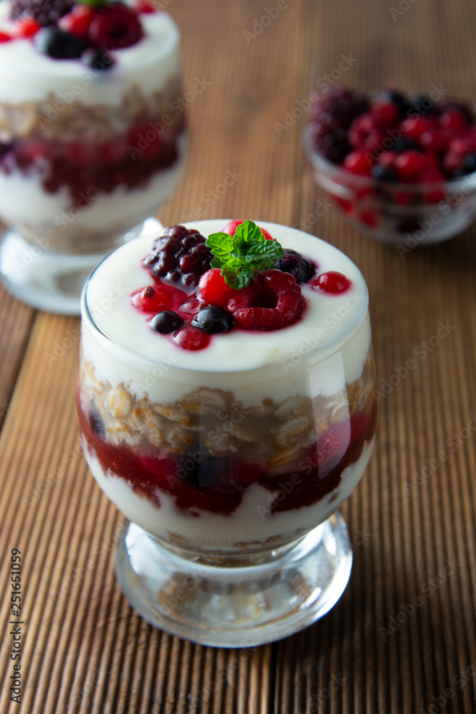Glass jar withovernight oats, granola and yogurt with berry, raspberries and blackberries on wooden cutting board over wooden background. Healthy food. Glass jar withovernight oats, granola and yogurt with berry, raspberries and blackberries on wooden cutting board over wooden background. Healthy food.