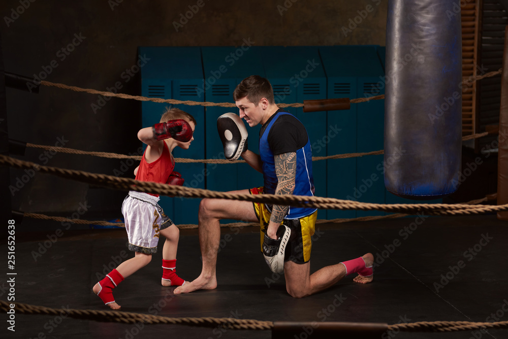 Trainer teaching a kid how to hit punches. Kid wearing boxing gloves