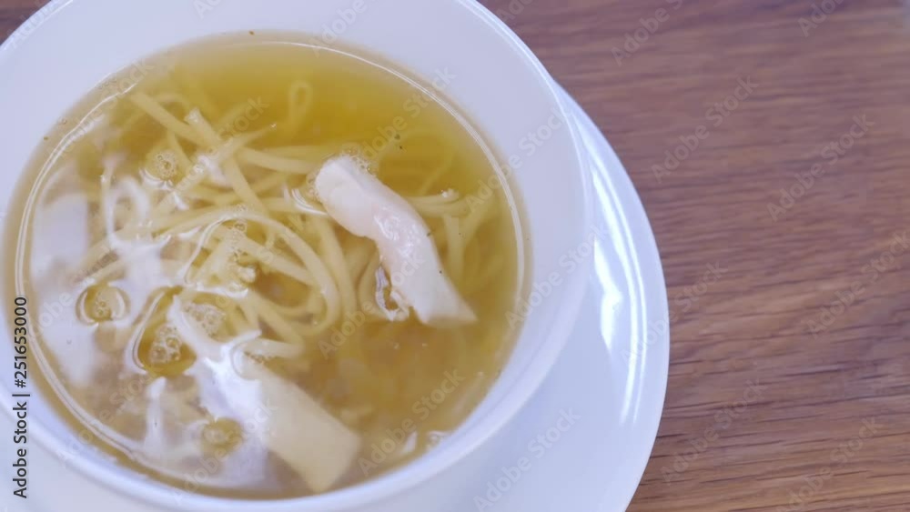 Cook serves chicken soup with noodles in white bowl. Puts pieces of chicken, hands close-up. Cook serves chicken soup with noodles in white bowl. Puts pieces of chicken, hands close-up.