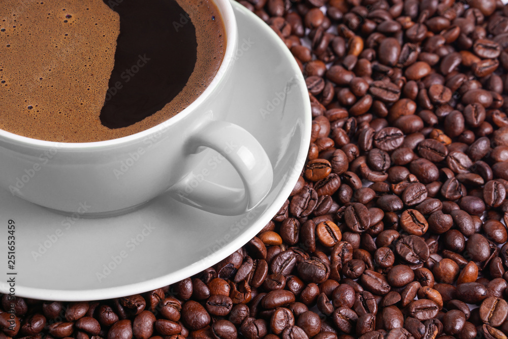 Fototapeta premium Coffee in gray cup on a table surrounded by coffee beans.