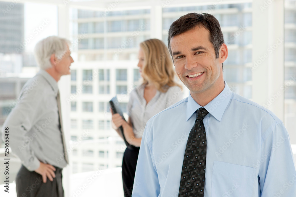 Corporate executive businessman portrait - business partners talking in background Corporate executive businessman portrait - business partners talking in background
