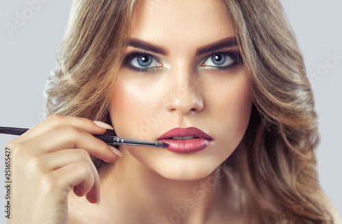 The make-up artist paints the lips of a beautiful woman, completes the day's make-up in the beauty salon. Professional skin care.