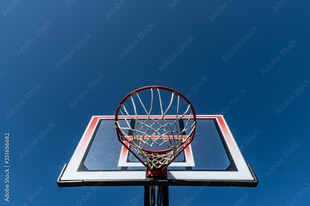 Transparent rectangular fiberglass backboard and red basketball hoop/ rim & white net/ netting. Outdoor urban school basket ball court. Children's community street sports park. Team sport competition. Transparent rectangular fiberglass backboard and red basketball hoop/ rim & white net/ netting. Outdoor urban school basket ball court. Children's community street sports park. Team sport competition.