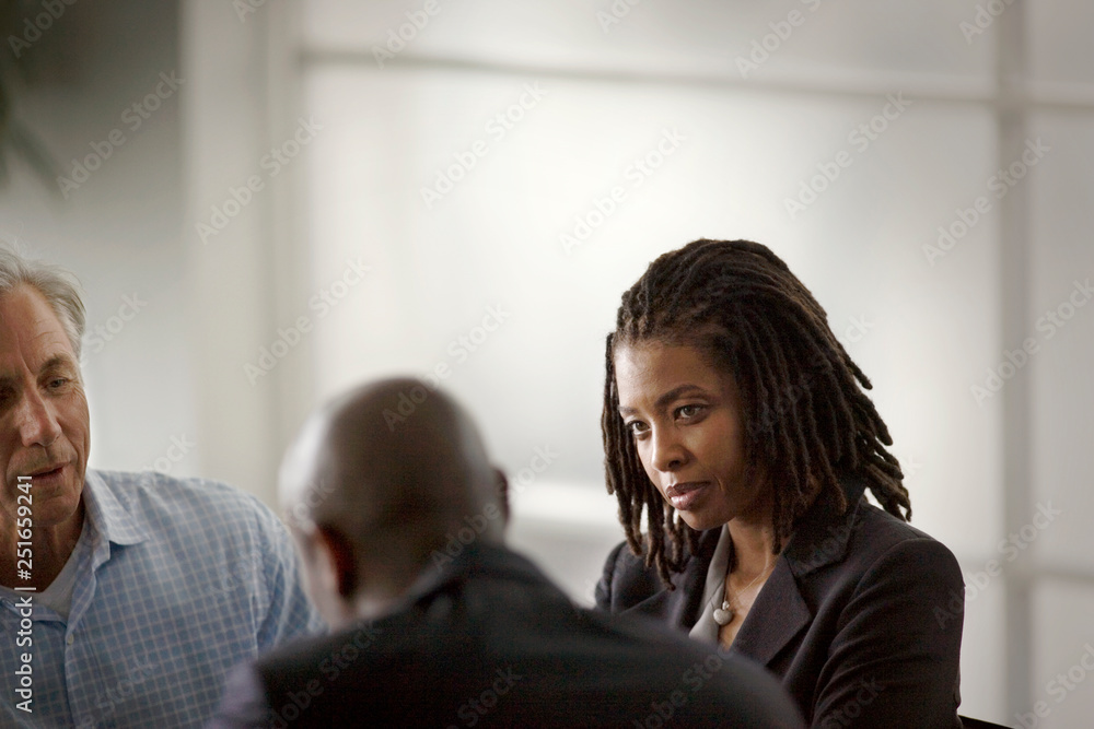 Mid-adult business woman sitting with colleague and a mature adult man in an office. Mid-adult business woman sitting with colleague and a mature adult man in an office.
