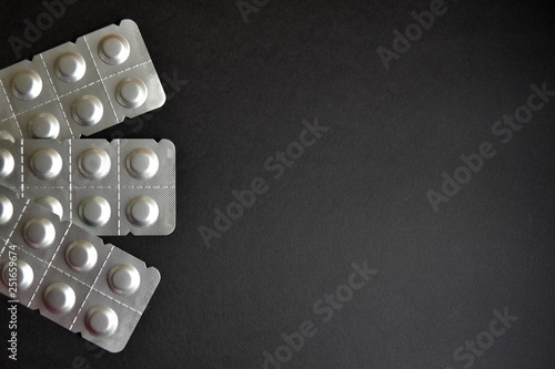 Round medical tablets in three packs, tablets packed in blisters on the left side with copyspace on black background