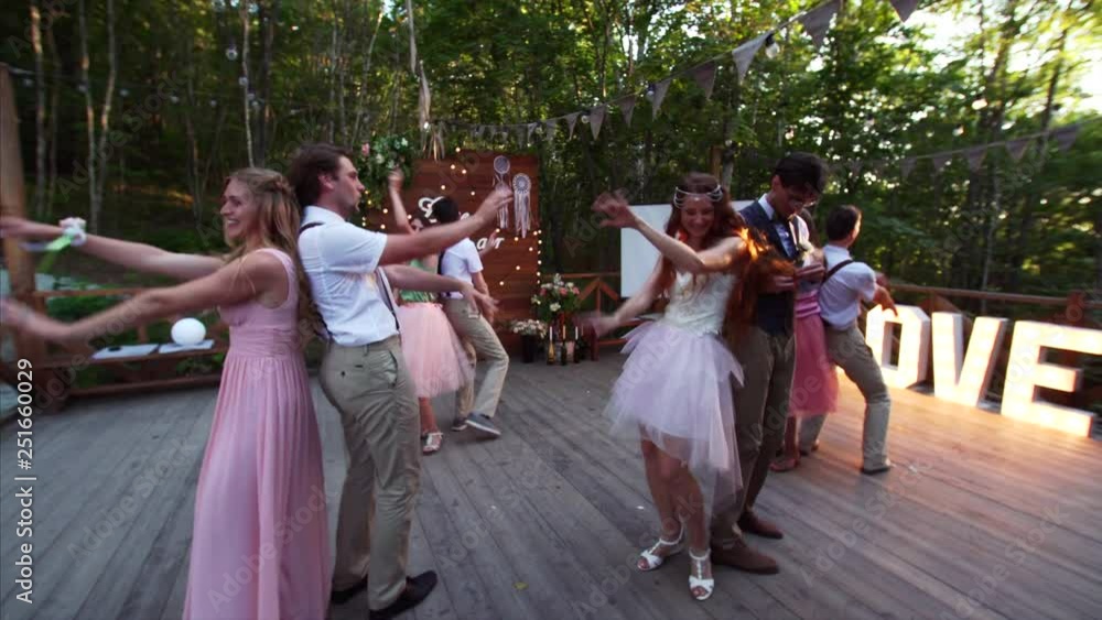 Bride, groom and their maids of honor and best men are performing lively dance on the stage in the park in front of guests. Nice summer evening Bride, groom and their maids of honor and best men are performing lively dance on the stage in the park in front of guests. Nice summer evening