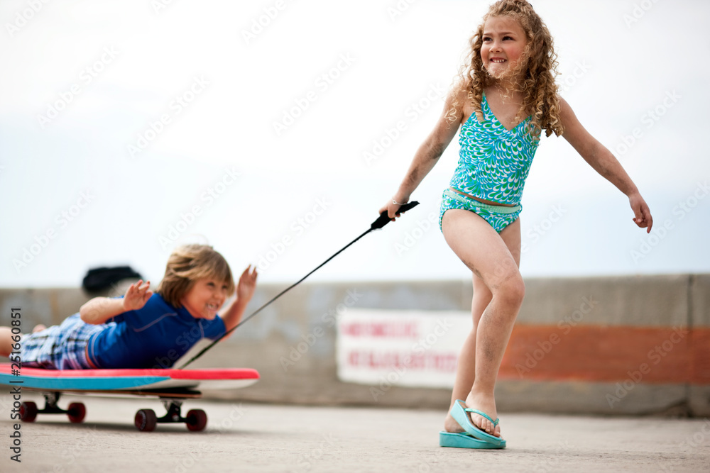 Young girl pulling her brother on a makeshift wagon made from a
