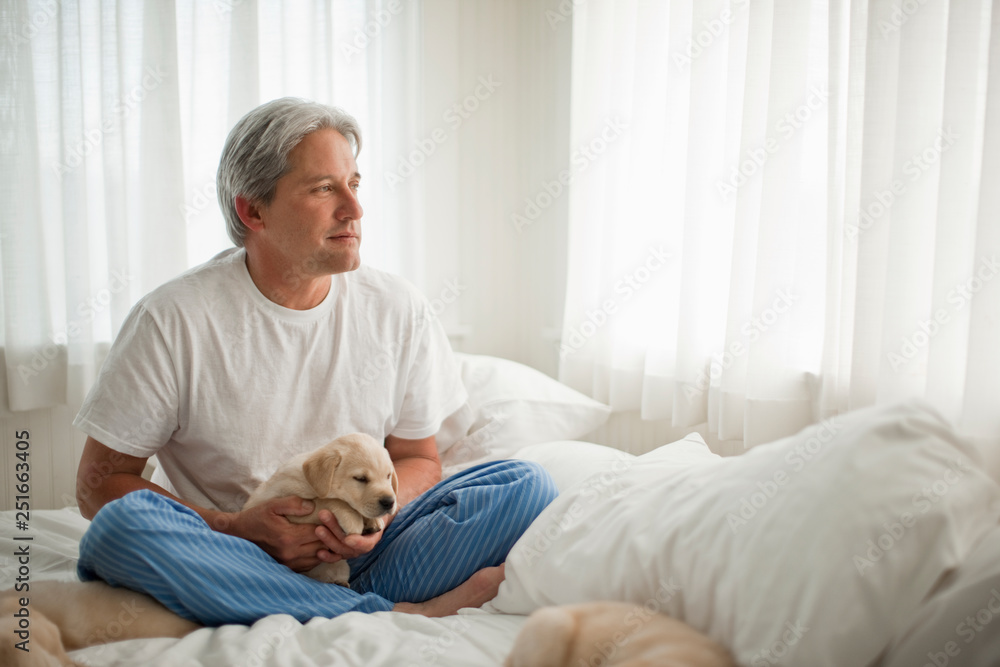 Middle aged man holding Labrador puppy while sitting on his bed. Middle aged man holding Labrador puppy while sitting on his bed.