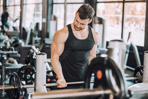 Muscular man working out in gym doing exercises with barbell at biceps