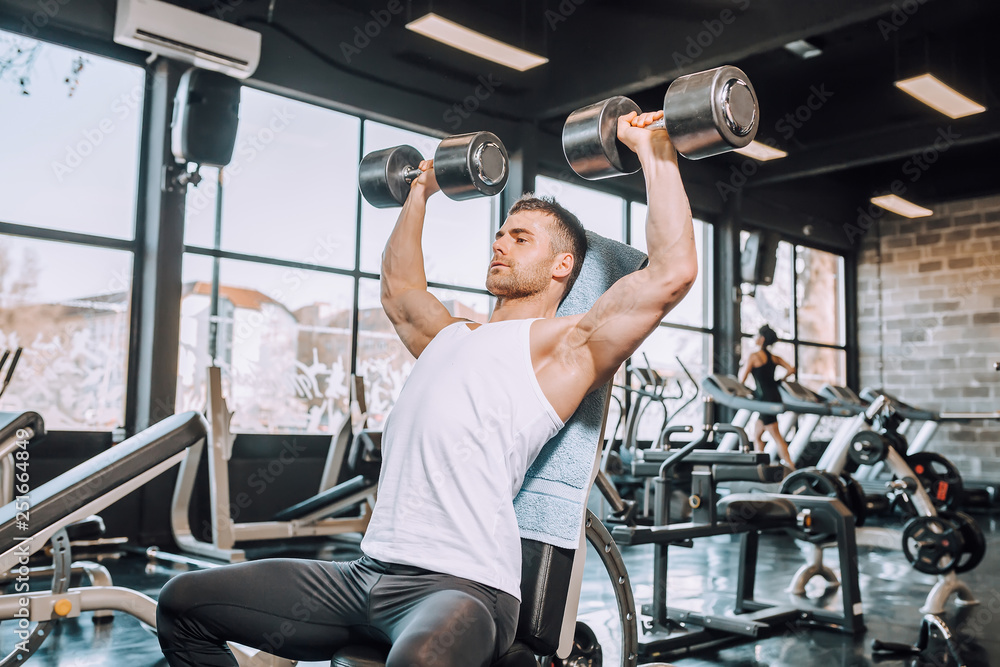 Muscular bodybuilder guy doing exercises with dumbbells Muscular bodybuilder guy doing exercises with dumbbells