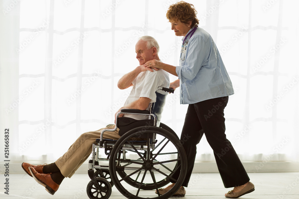 Mature doctor pushing an elderly patient in a wheelchair. Mature doctor pushing an elderly patient in a wheelchair.