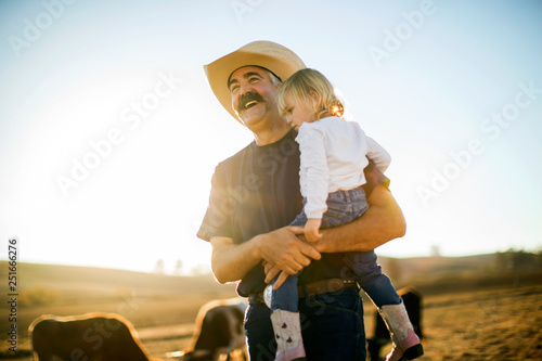 Smiling cowboy carrying his daughter on ranch photo