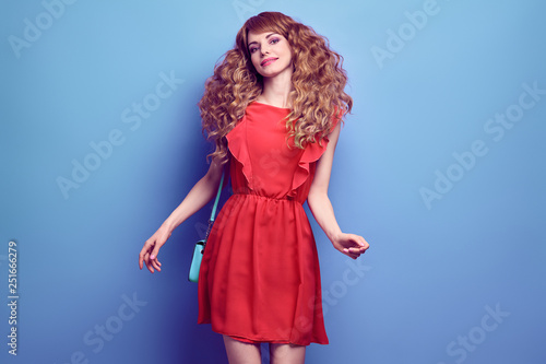 Young pretty girl having fun Smiling. Beautiful easy-going woman in Stylish coral summer dress, Trendy curly hairstyle, makeup, fashionable handbag. Inspired happy model dance in Studio