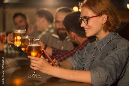Woman with ginger hair posing in beer pub. Beautiful female client smiling  holding beer glasses in hands and resting. Concept of weekend.