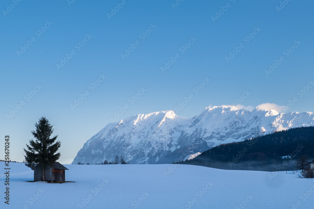 Obraz premium Snow covered hut on field with mountains Grimming, Schartenspitze, Steinfeldspitze