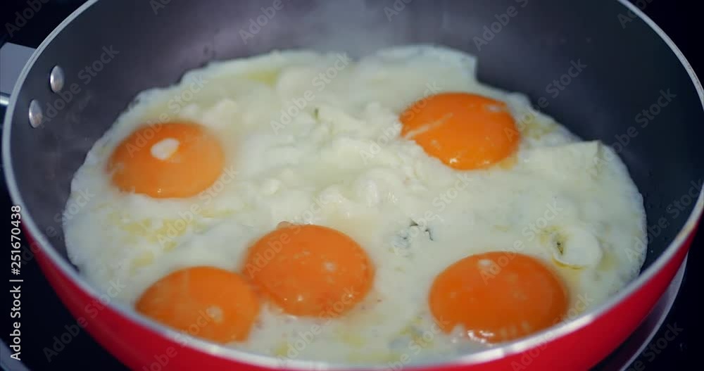 The Chef Prepares Frying Eggs, Cook in Butter, Seasoned With Salt and Black Pepper and Green Onions in a Small Red Pan. Concept of Healthy Eating. The Chef Prepares Frying Eggs, Cook in Butter, Seasoned With Salt and Black Pepper and Green Onions in a Small Red Pan. Concept of Healthy Eating.