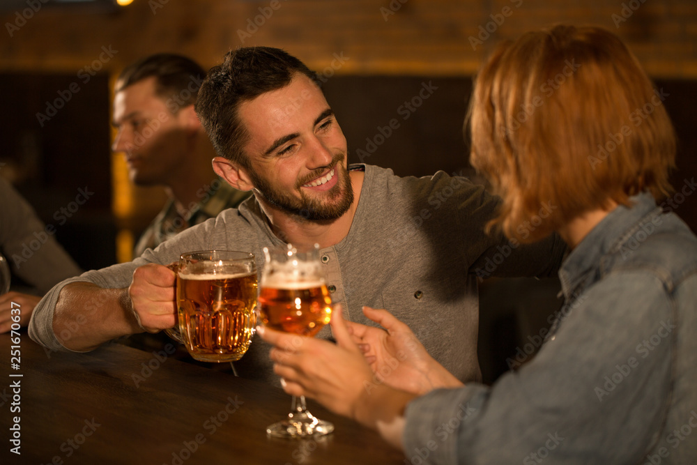 Handsome bearded man smiling and looking at woman. Friends talking, communicating and enjoying weekends in beer pub. Clients of bar holding beer glasses, resting and hanging out.