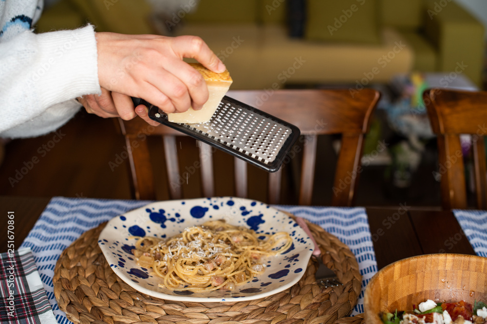 woman hands grating parmesan cheese on pasta carbonara