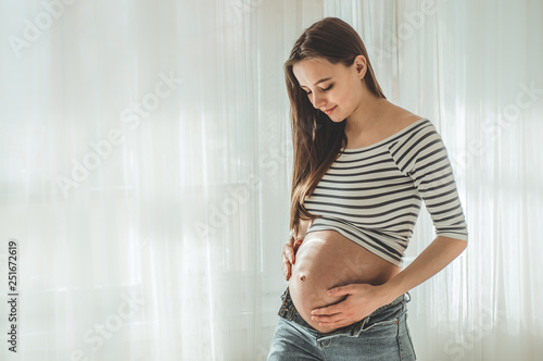 Happy Attractive pregnant woman standing near the window and holding her belly Free Download Happy Attractive pregnant woman standing near the window and holding her belly - GFXLoad