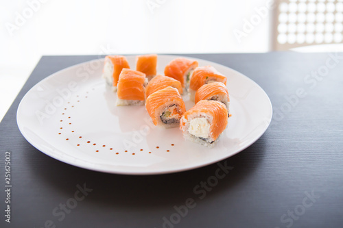 Sushi roll with salmon, philadelphia on a white plate on a black background top view.