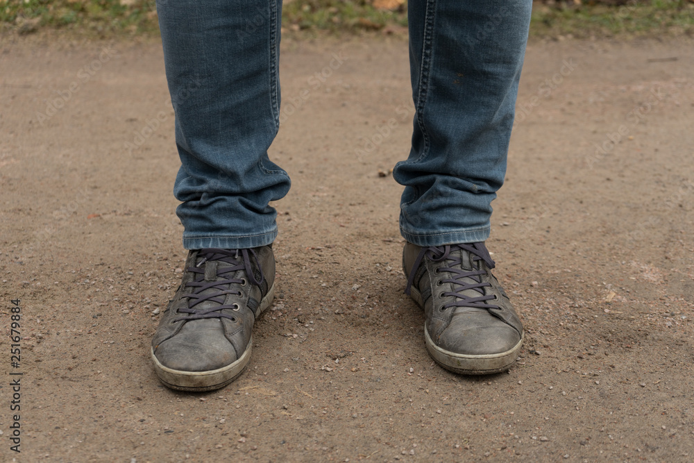 Two man feet with shoes on and blue jeans. Feet standing on the dirt path with grey shoes. Two man feet with shoes on and blue jeans. Feet standing on the dirt path with grey shoes.