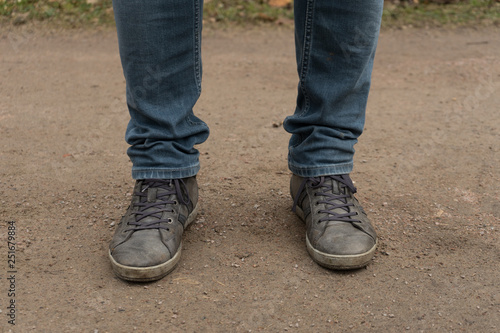 Two man feet with shoes on and blue jeans. Feet standing on the dirt path with grey shoes.