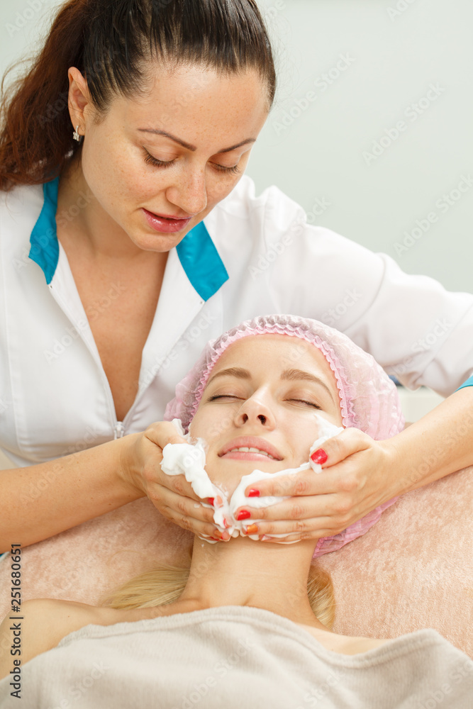 Attractive woman lying on couch and relaxing during beauty procedure in salon. Professional cosmetologist cleaning face of young patient after rejuvenation mask. Skin care concept. Attractive woman lying on couch and relaxing during beauty procedure in salon. Professional cosmetologist cleaning face of young patient after rejuvenation mask. Skin care concept.