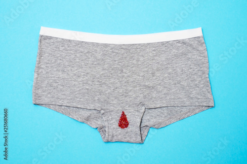 Red drop from beads on pants on blue background. Menstruation period photo