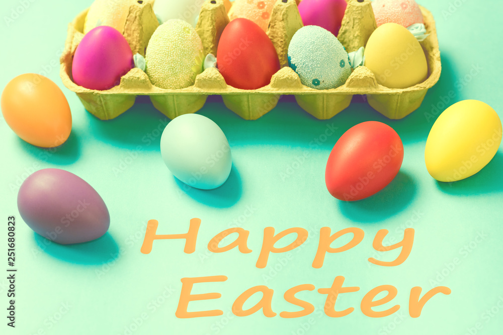 Bright Easter eggs lie in a box on a blue background. Inscription happy easter. Space for text. Easter ideas. Toned image. Bright Easter eggs lie in a box on a blue background. Inscription happy easter. Space for text. Easter ideas. Toned image.