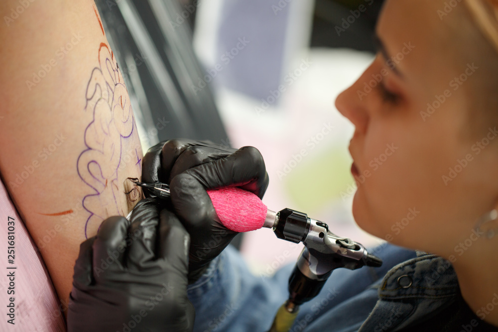 Professional tattoo master concentrated on making tattoo on client's body.  Tattooer in black gloves using special tattoo machine with needle.  Tattooist drawing picture on skin. Stock Photo | Adobe Stock